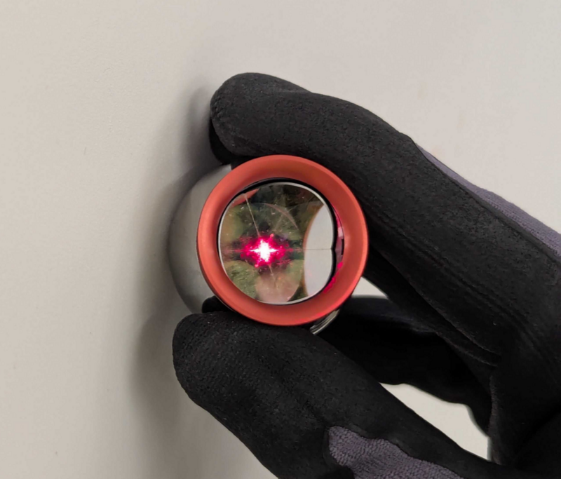 Hand holding the reflector flush against a wall surface, with the tracker laser visible on the reflector.