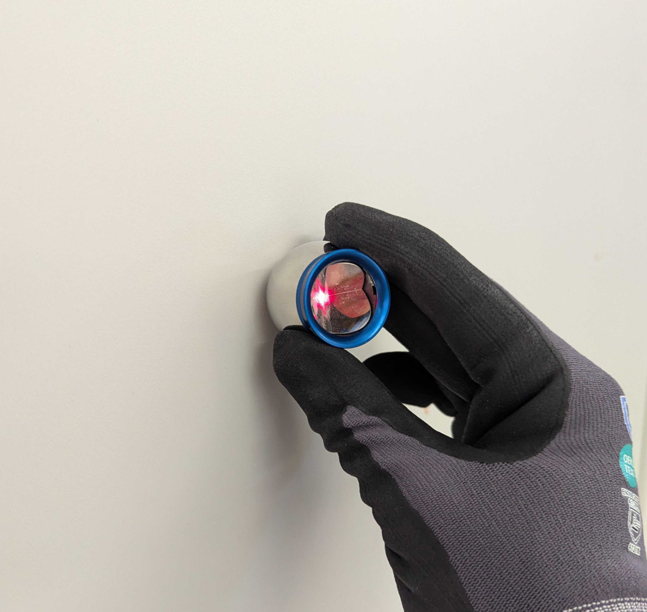 Hand holding the reflector flush against a wall surface, with the tracker laser visible on the reflector.